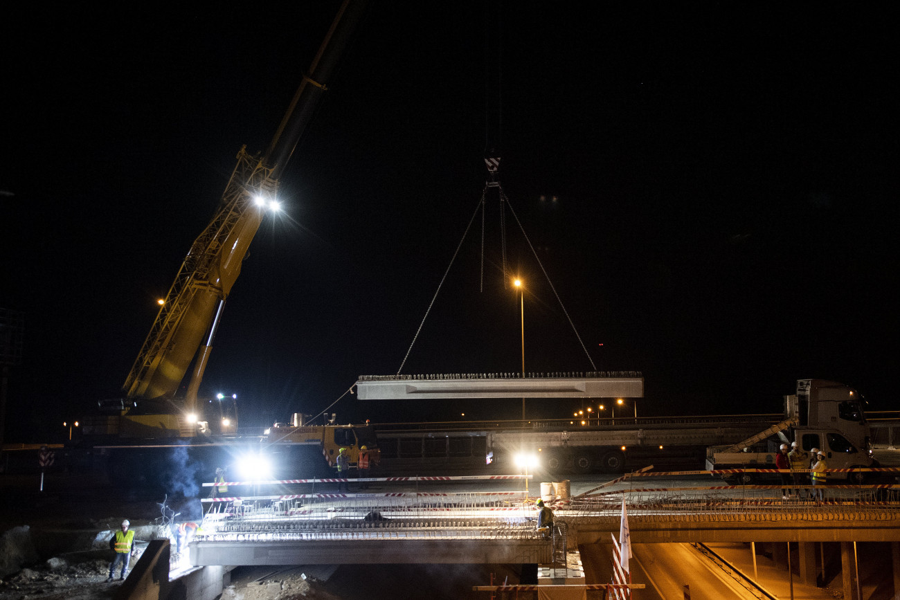 Szigetszentmiklós, 2020. április 18.
Daru segítségével beemelik az egyik hídgerendát a STRABAG Építő Kft. munkatársai a meglévő háromnyílású, négytámaszú híd kiszélesítésének építkezésén, az M0-ás gyorsforgalmi út déli szektora korszerűsítési munkálatain Szigetszentmiklóson 2020. április 17-én. A három nyílásközbe egy 100 tonna teherbírású autódaruval összesen 12 gerendát emelnek be, amelyeknek összsúlya meghaladja a 89 tonnát. A kiszélesítéssel a hídon eggyel több forgalmi sávon haladhat a forgalom, a létrejövő sávok 3,75 méter szélesek lesznek.
MTI/Illyés Tibor
