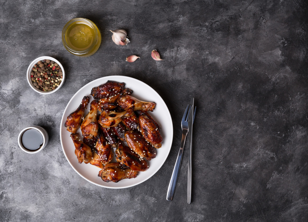 Spicy chicken wings with teriyaki sauce and sesame seeds in a white plate on a dark background.Top view with place for text.