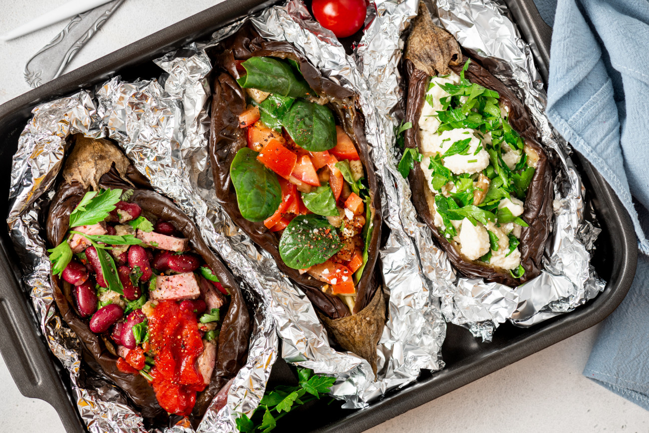 Stuffed eggplant in foil. Baked eggplants with various fillings on a baking sheet, top view.